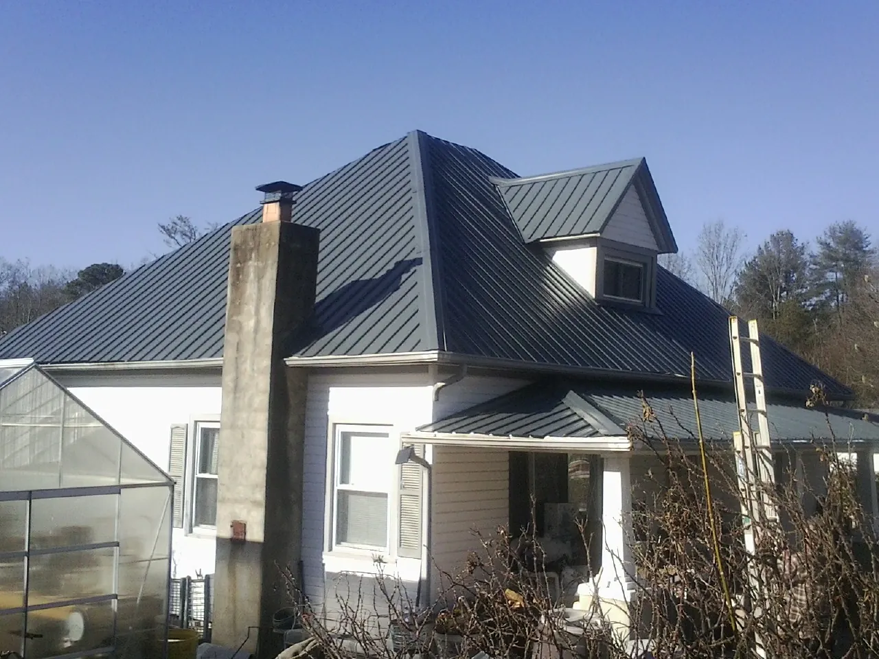 Dark blue standing seam metal roof on a white farmhouse with dormer — Slate & Tile Roof Repair by Roofing Brothers in Richmondville