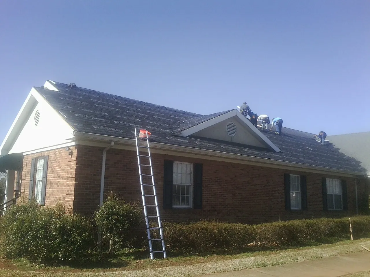 Crew tearing shingles off a brick ranch roof with a ladder set — Metal Roof Repair work by our crew in Richmondville