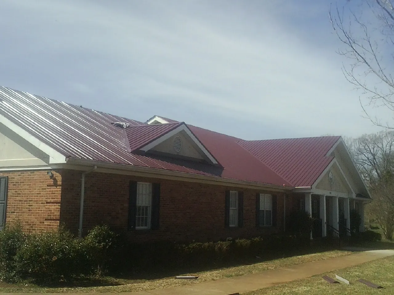 Red metal roof with gabled entries on a long brick building, from a Hail Damage Roof Repair job in Richmondville