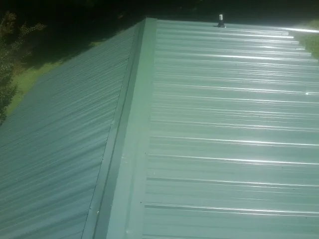 New green metal panels meeting at the ridge of a roof — Flat Roof Repair work by our crew in Richmondville