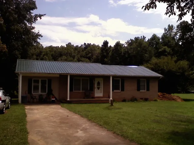 Dark green metal roof on a brick ranch with a covered porch in Richmondville