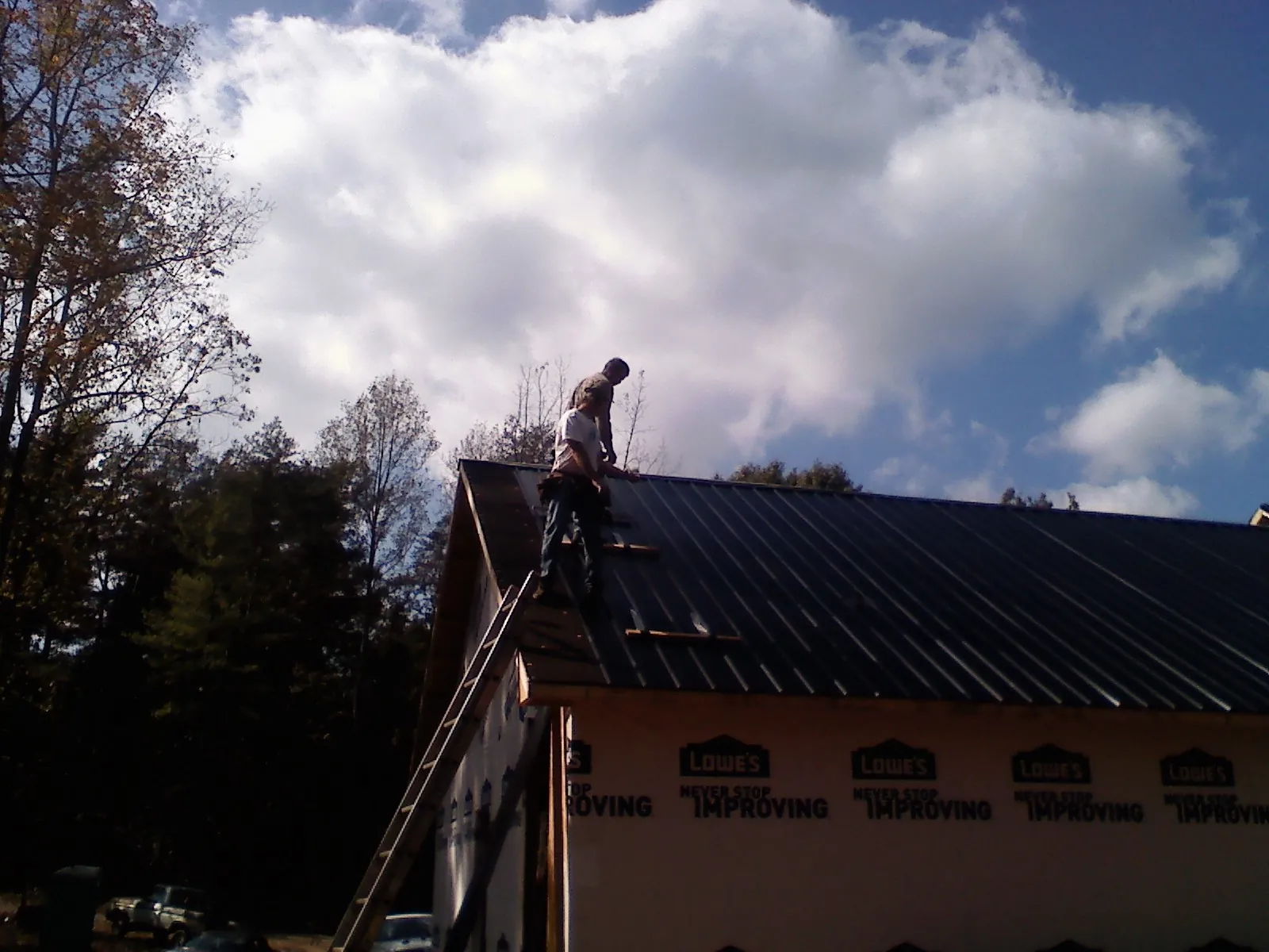 Roofer fastening dark metal panels high against a cloudy sky, from a Roof Inspection job in Richmondville