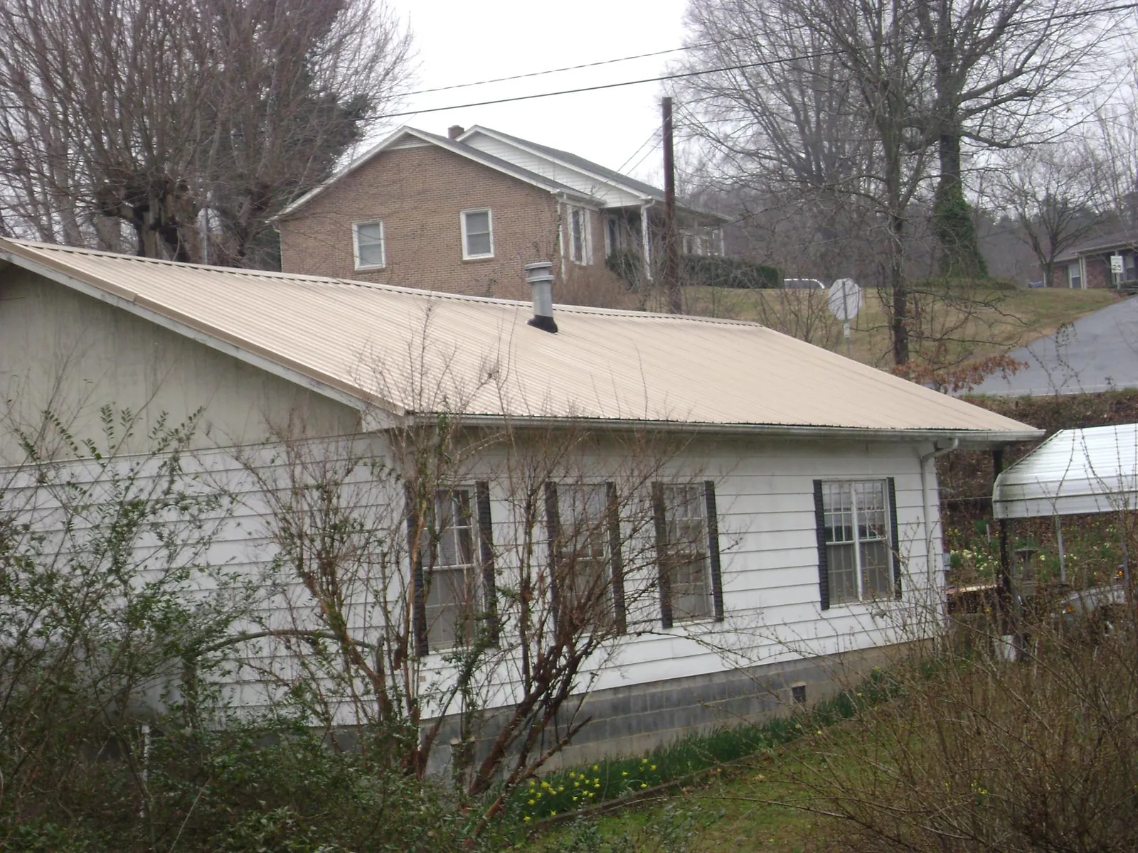 Tan metal roof on a white sided house set into a hillside — Commercial Roofing by Roofing Brothers in Richmondville