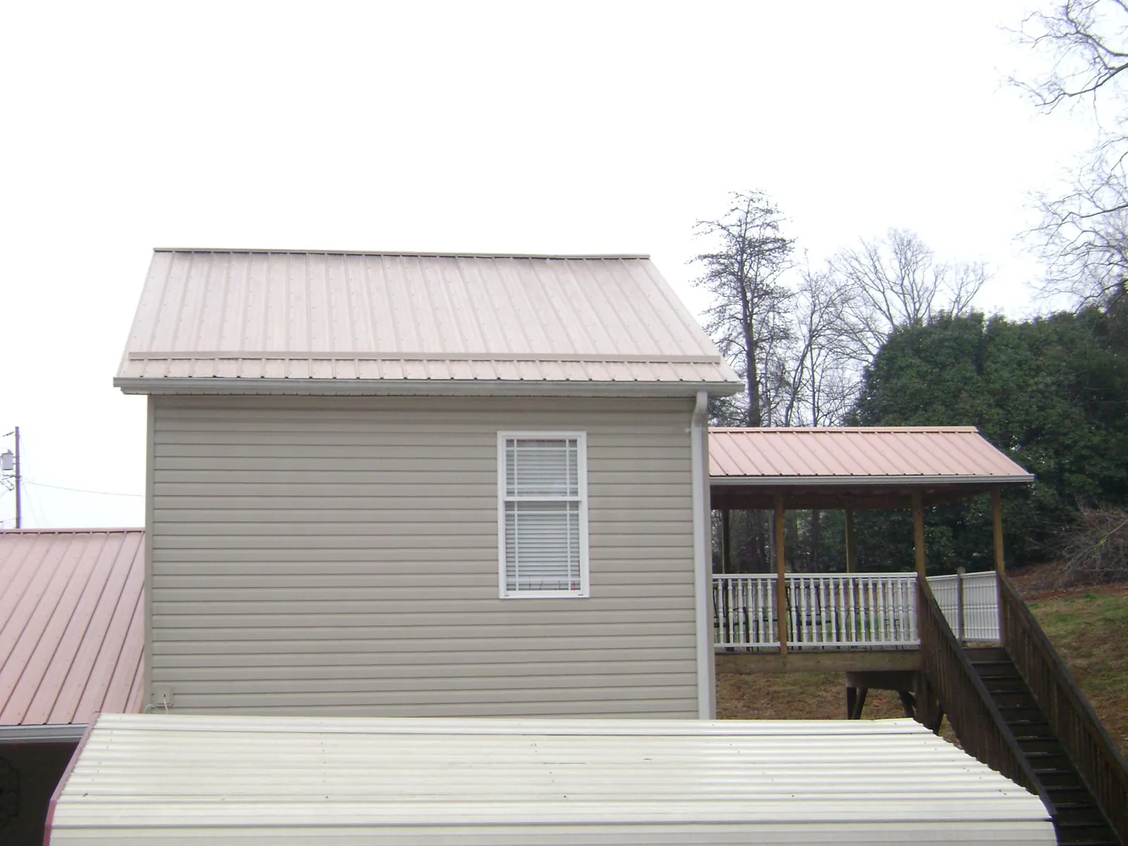 Tan metal roofs on a two story addition and attached porch, from a Roof Replacement job in Richmondville